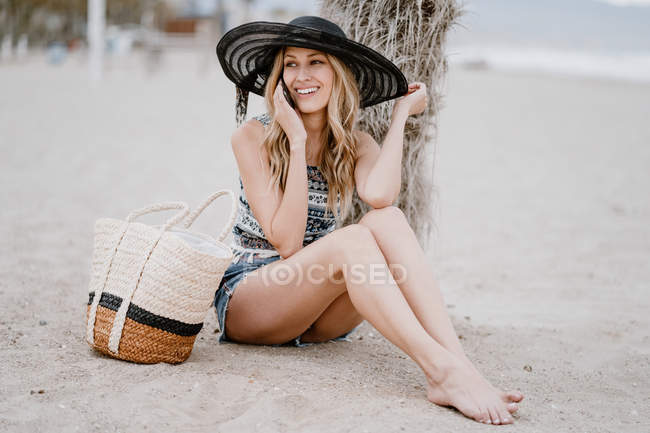 Joven atractiva hembra con el pelo largo relajándose en la orilla del mar y hablando por teléfono móvil en el día de verano - foto de stock