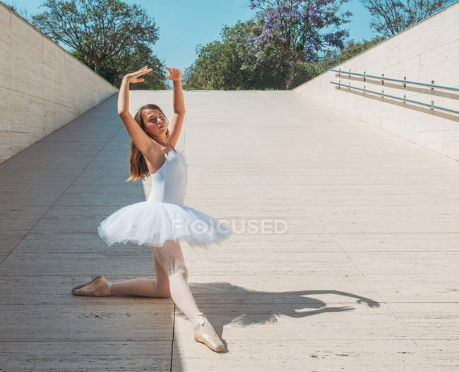 Ballerina tritt bei strahlendem Sonnenschein mit erhobenen Händen und streckenden Beinen draußen auf — Stockfoto