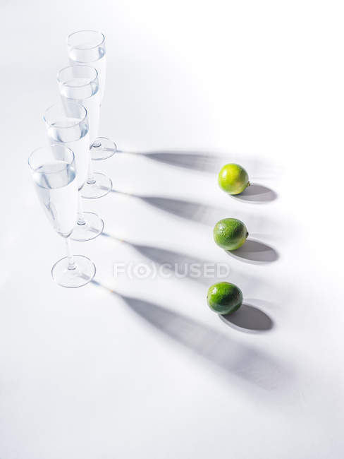 Контрастные тени из стаканов воды и зеленых спелых лаймов на белом фоне — стоковое фото