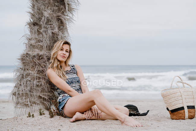 Porträt einer jungen schönen blonden Frau, die am Strand sitzt und in die Kamera blickt — Stockfoto