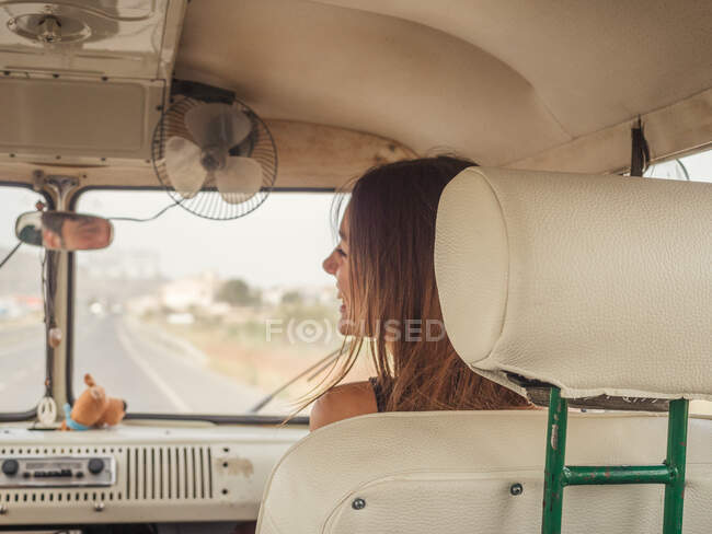 Вид сзади на молодую улыбающуюся женщину в солнечных очках, сидящую впереди в машине и отворачивающуюся — стоковое фото