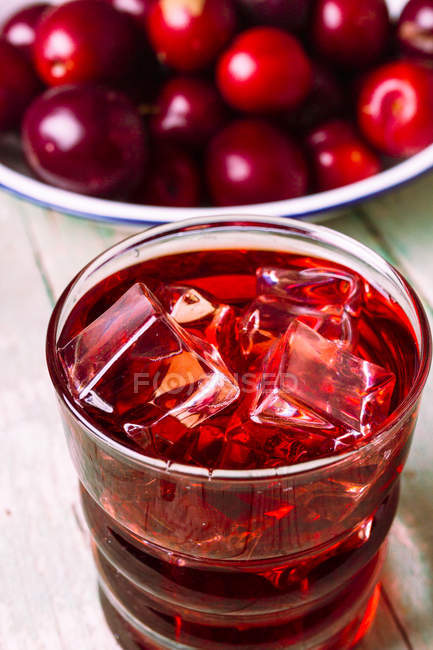 Glass of cold red beverage placed on wooden table near bowl of fresh red fruits — Stock Photo