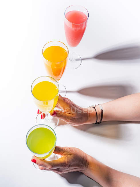 Mãos femininas segurando copos de vidro de suco no fundo branco — Fotografia de Stock