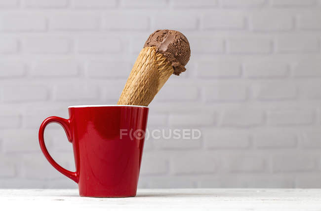 Cono de helado de chocolate en taza roja contra la pared de ladrillo blanco - foto de stock