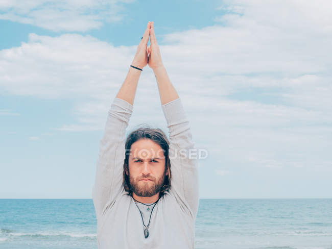 Sportif homme barbu formation sur le bord de mer tranquille et faire du yoga asana contre la mer bleue et le ciel — Photo de stock