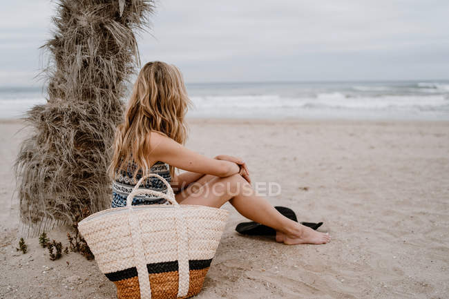 Вид сбоку на молодую красивую блондинку, сидящую на пляже и отводящую взгляд — стоковое фото