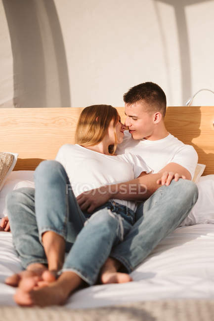 Молода романтична пара в білих футболках і джинсах лежить і обіймається в спальні гламуру — стокове фото