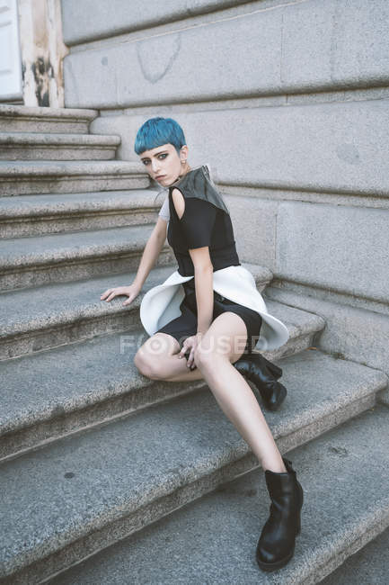 Jeune femme aux cheveux bleus courts portant une robe informelle tendance et posant sur les marches de la rue — Photo de stock