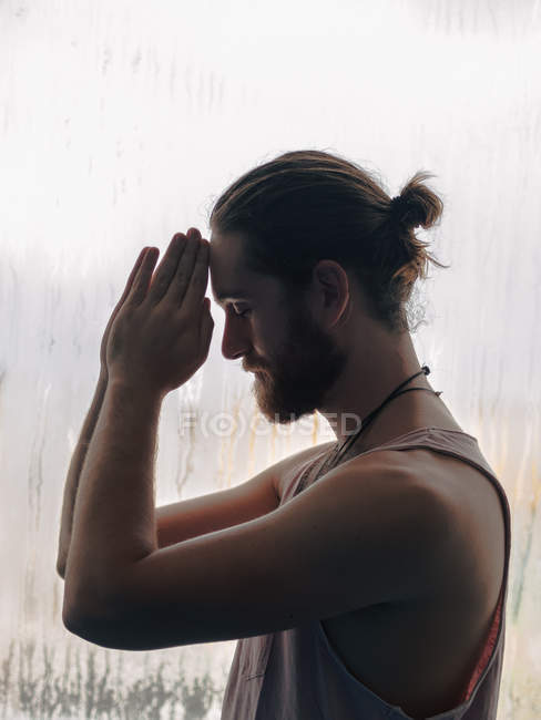 Relaxed thoughtful man with praying hands in forehead near steamy windows with closed eyes — Stock Photo