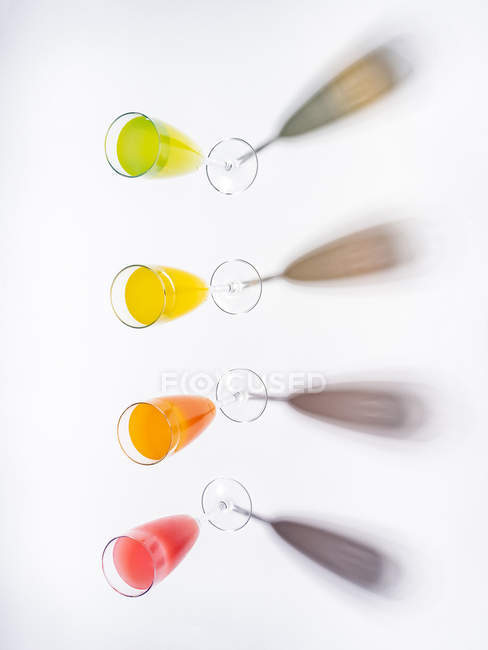 Контрастные тени из стаканов аппетитных аппетитных оранжево-желтых зеленых напитков на белом фоне — стоковое фото