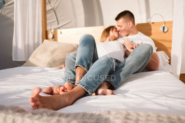 Young romantic couple in white t-shirts and jeans lying and hugging in bedroom of glamping — Stock Photo