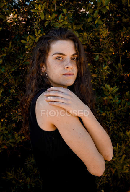 Portrait of young female standing against bush background and looking at camera — Stock Photo