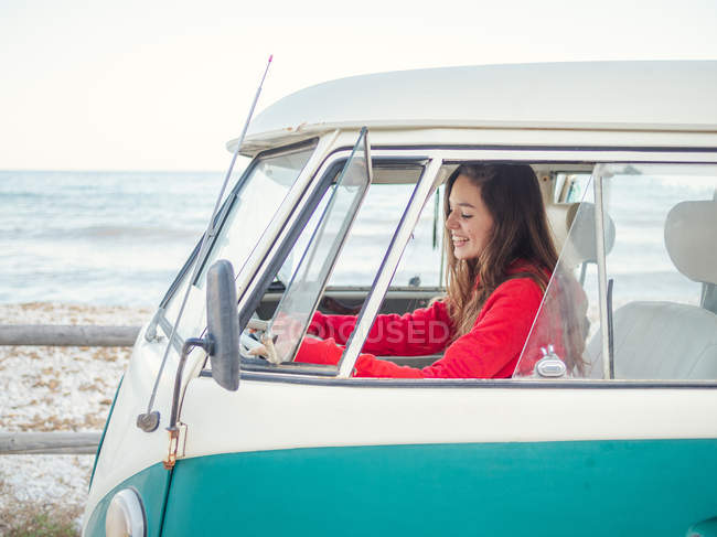 Side view of young woman driving a vintage van at seaside — Stock Photo