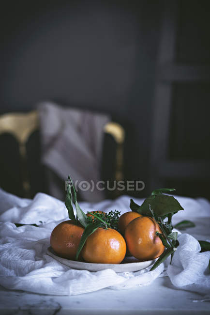 Стиглі помаранчеві мандарини на тарілці з тканиною на білій мармуровій стільниці — стокове фото