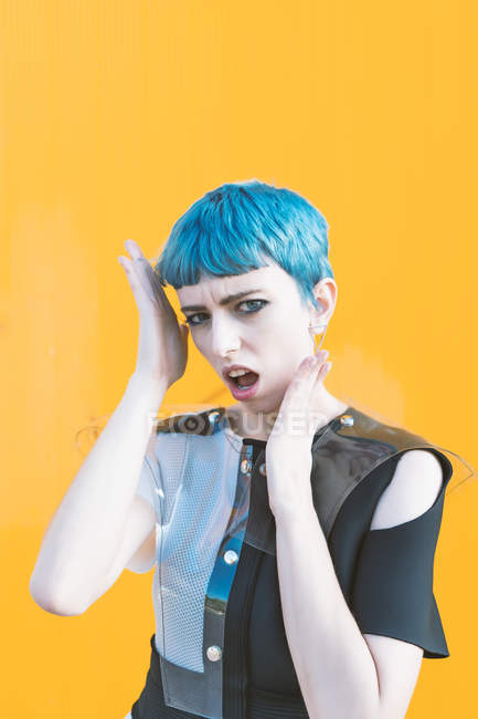 Jeune femme en robe futuriste tendance sur le trottoir contre un mur jaune vif — Photo de stock