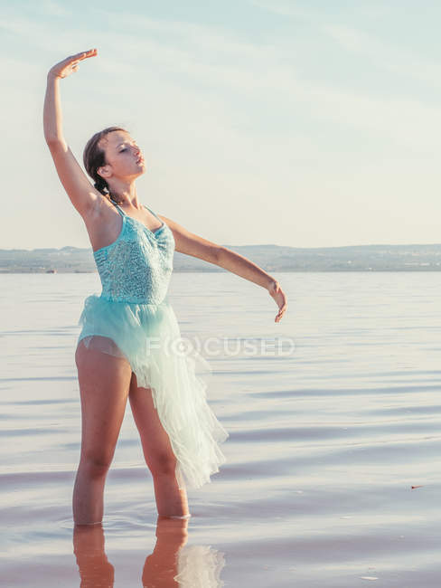Ballerina  performing with raising hands in wavy water in bright sunny day — Stock Photo