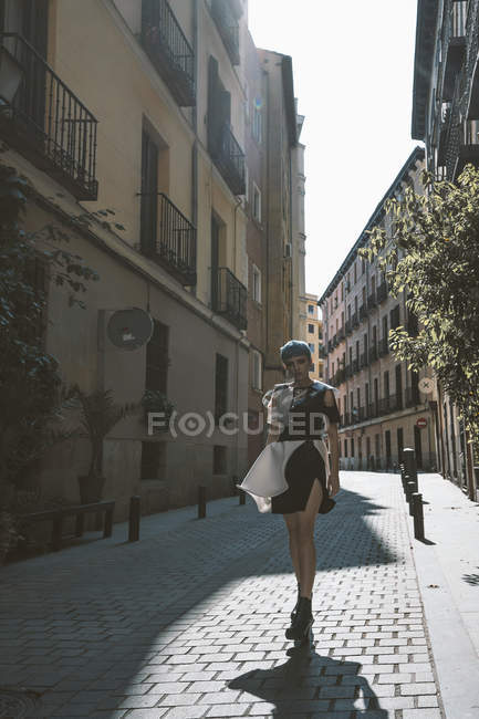 Молода жінка в футуристичній сукні стоїть на вулиці проти старої будівлі на сонячному світлі — стокове фото