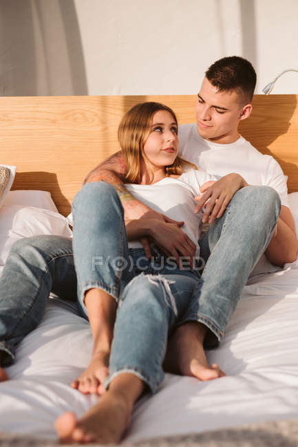 Romantic couple in white t-shirts and jeans lying and hugging in bedroom of glamping — Stock Photo