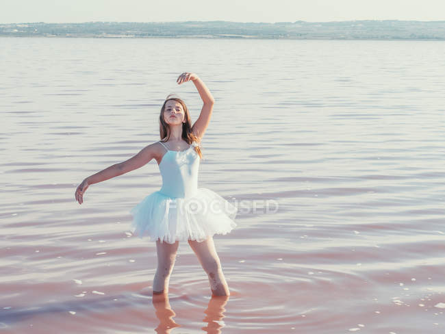 Bailarina realizando con levantamiento de manos en agua ondulada en día soleado brillante - foto de stock