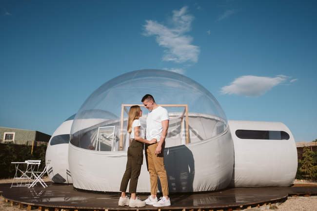 Side view of passionate man and young woman while standing in front of romantic transparent glamping — Stock Photo