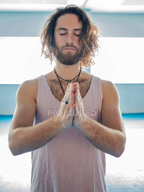 Bearded man in sportswear standing on one leg with prayer hands looking away on blue floor in studio — Stock Photo