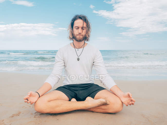 Sportive bearded man training on tranquil seashore and doing yoga asana against blue sea and sky — Stock Photo
