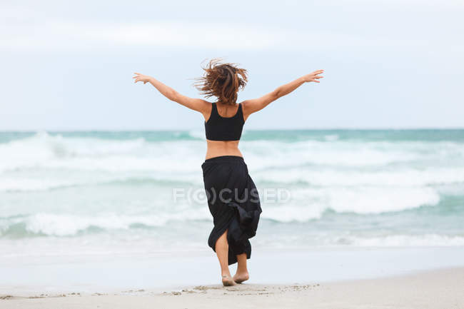 Rückansicht einer fröhlichen Frau, die am Meer tanzt — Stockfoto