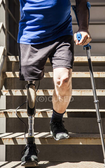 Uomo irriconoscibile amputato con stampelle che testano la sua nuova protesi alle gambe scendendo le scale — Foto stock