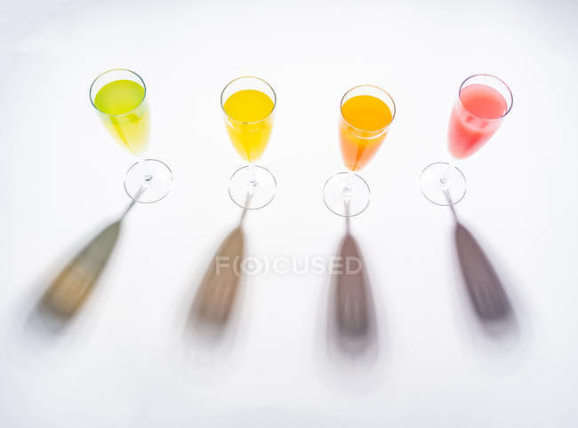 Contrasting shadows from glasses of juicy appetizing orange red yellow green drinks on white background — Stock Photo
