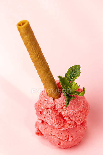 Stacked ice cream scoops decorated with mint leaves and wafer roll on pink background — Fotografia de Stock