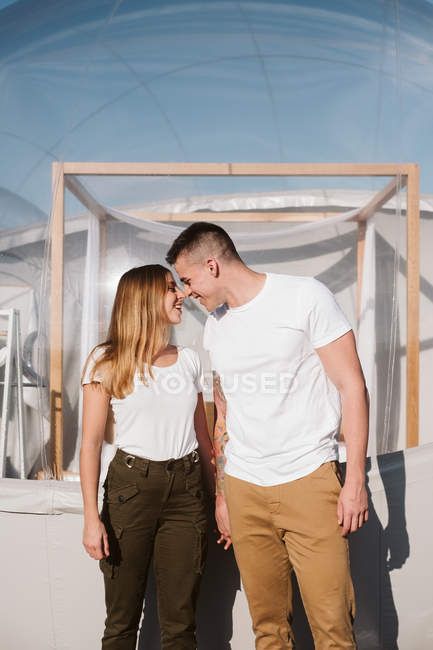 Vista lateral del hombre apasionado y la mujer joven, mientras que de pie delante de glamping transparente romántico - foto de stock