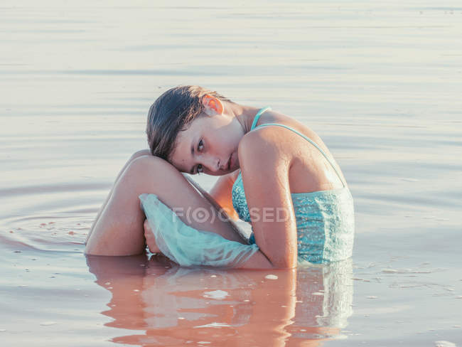 Thoughtful girl in dress sitting in ripple water — Stock Photo