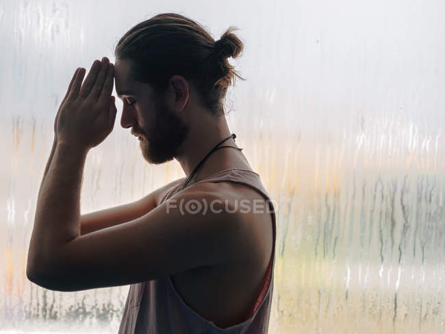 Relaxed thoughtful man with praying hands in forehead near steamy windows with closed eyes — Stock Photo