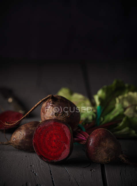 Dark red sugar beetroots on stems with green leaves on black wooden background — Stock Photo