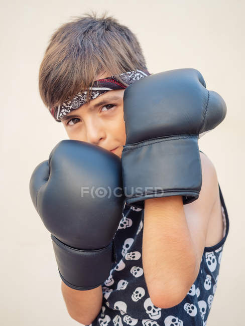 Serio chico concentrado en guantes de boxeo negro golpeando saco de boxeo con poder - foto de stock