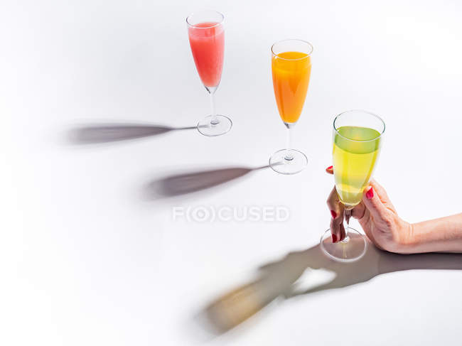 Mão feminina segurando vidro de vidro de suco no fundo branco — Fotografia de Stock