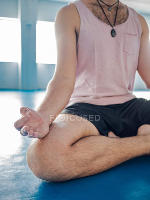 Image recadrée de l'homme en vêtements de sport avec les jambes croisées méditant sur le sol bleu avec des balles de gymnastique en studio — Photo de stock