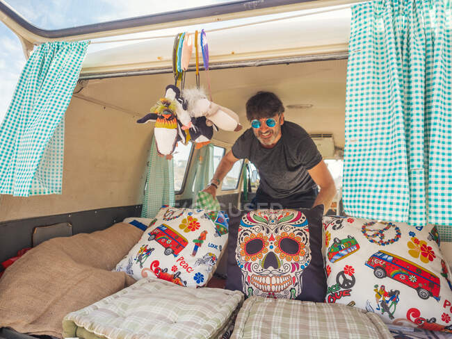 Smiling energetic man in sunglasses spreading cushions in cozy corner in traveling trailer — Stock Photo