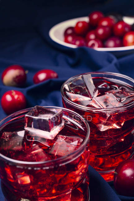 Glasses with cold red drink placed on blue fabric near bowl with ripe fruits — Stock Photo