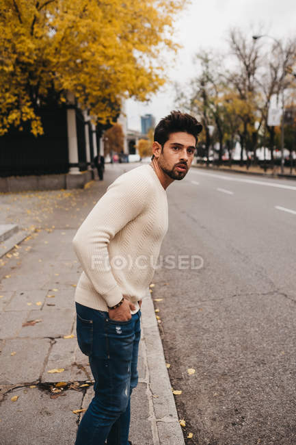 Модный мужчина в джинсах и свитере стоит с руками в карманах и ждет поездки — стоковое фото