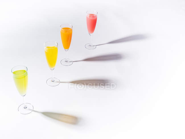 Контрастні тіні з келихів соковитих апетитних помаранчевих червоних жовтих зелених напоїв на білому тлі — стокове фото