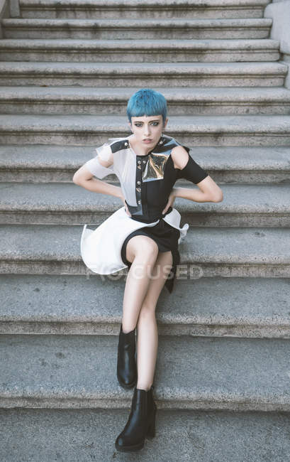 Giovane donna con i capelli corti blu indossa abito informale alla moda e posa su gradini di strada — Foto stock