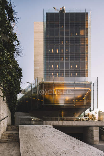 Arranha-céu de vidro elegante com estacionamento refletindo sol em dia brilhante no centro da cidade — Fotografia de Stock
