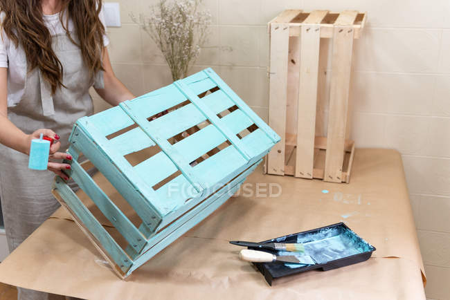 Крупним планом жінка фарбує дерев'яну коробку в синій колір з роликом — стокове фото