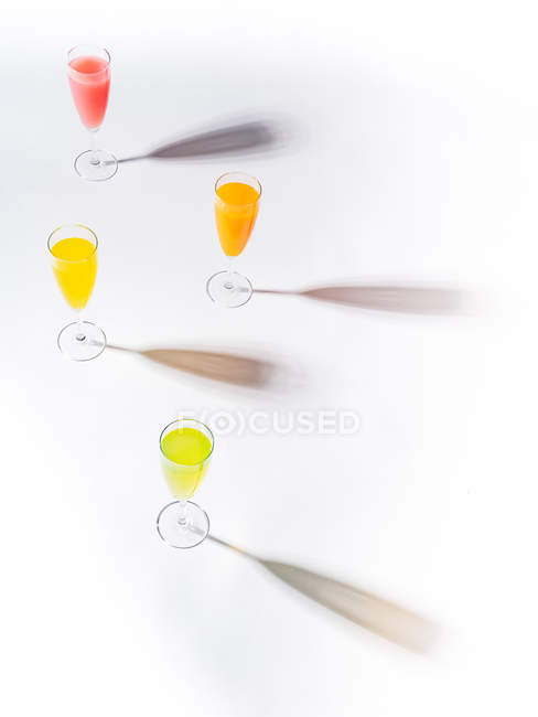Контрастні тіні з келихів соковитих апетитних помаранчевих червоних жовтих зелених напоїв на білому тлі — стокове фото