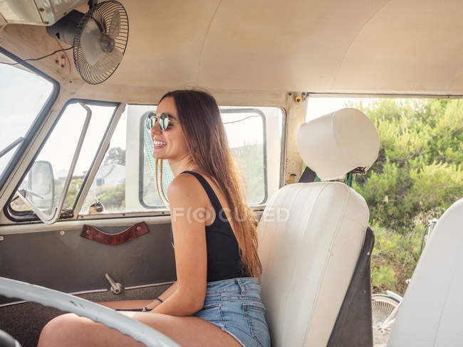 Вид сбоку улыбающейся молодой женщины в солнцезащитных очках, сидящей впереди в машине — стоковое фото