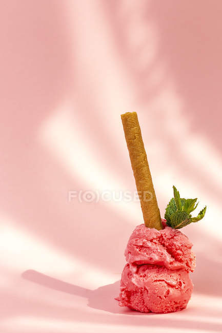 Stacked ice cream scoops decorated with mint leaves and wafer roll on pink background — Fotografia de Stock