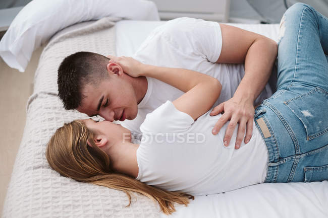 Romantisches Paar in weißen T-Shirts und Jeans im Glamping-Schlafzimmer liegend und umarmt — Stockfoto