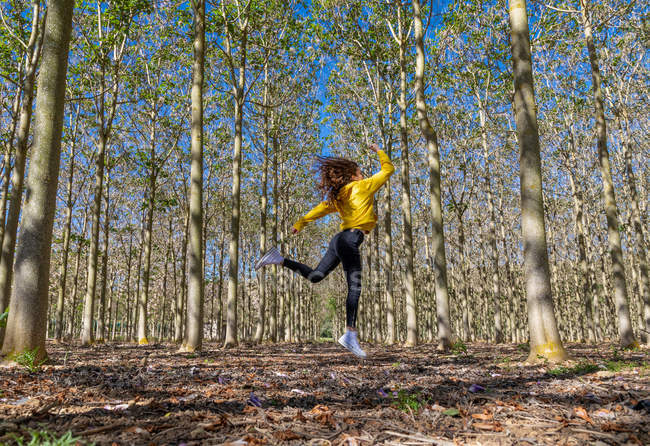 Jovem mulher em camisola amarela pulando na floresta — Fotografia de Stock
