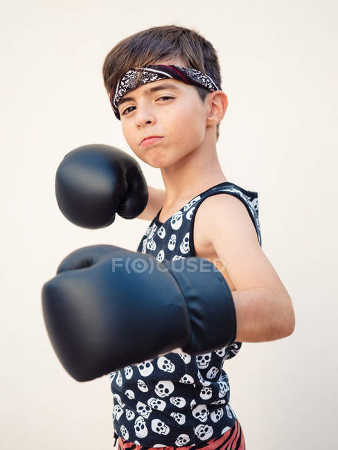 Серйозний концентрований хлопчик в чорних боксерських рукавичках б'є удар по камері — стокове фото